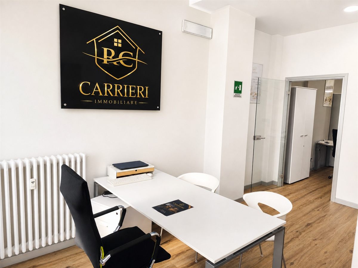 Area di accoglienza dell’agenzia Carrieri Immobiliare con tavolo riunioni e vista sugli uffici interni