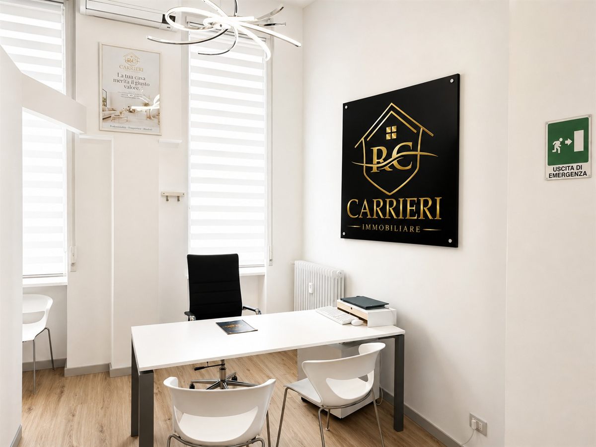 Postazione di lavoro dell’agenzia con scrivania bianca, sedute per i clienti e pannello dorato Carrieri Immobiliare